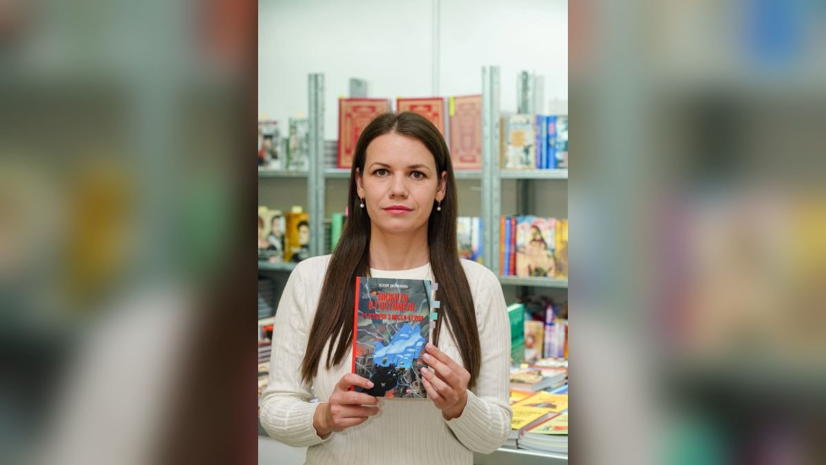 Ксенія Дворнікова тримає книгу «Вижити в Гостомелі: 21 історія з міста-героя» на тлі книжкових полиць
