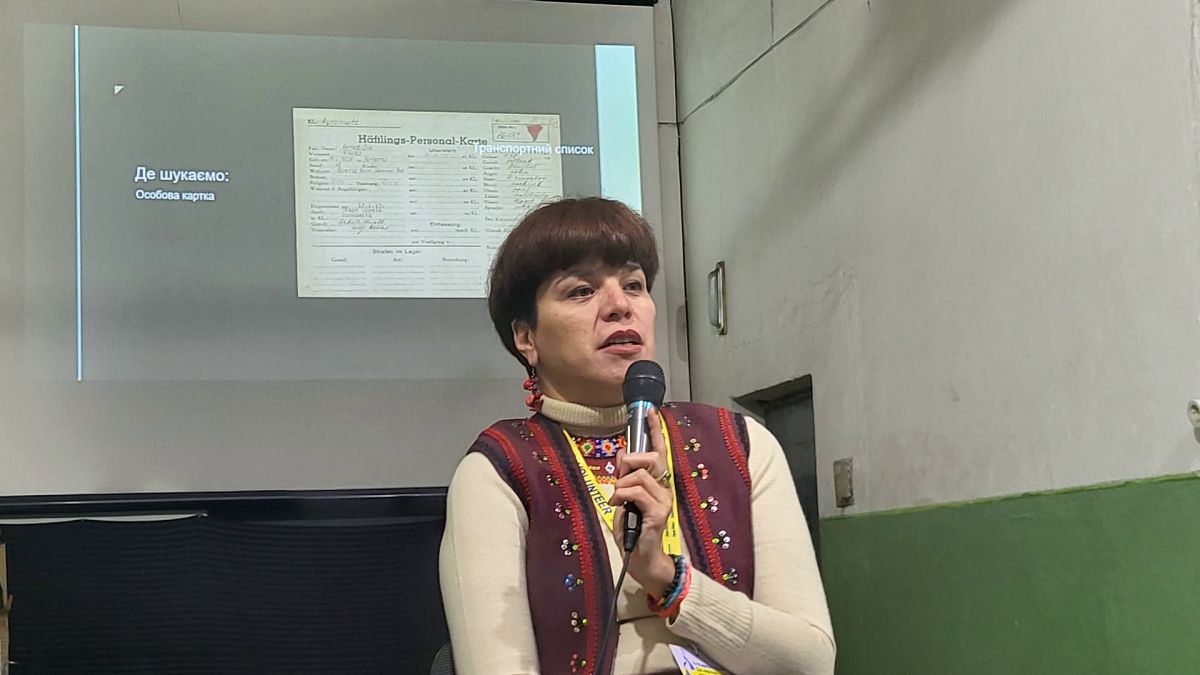 Олеся Ісаюк виступає з мікрофоном на лекції про ідентифікацію українців у списках в'язнів Аушвіцу