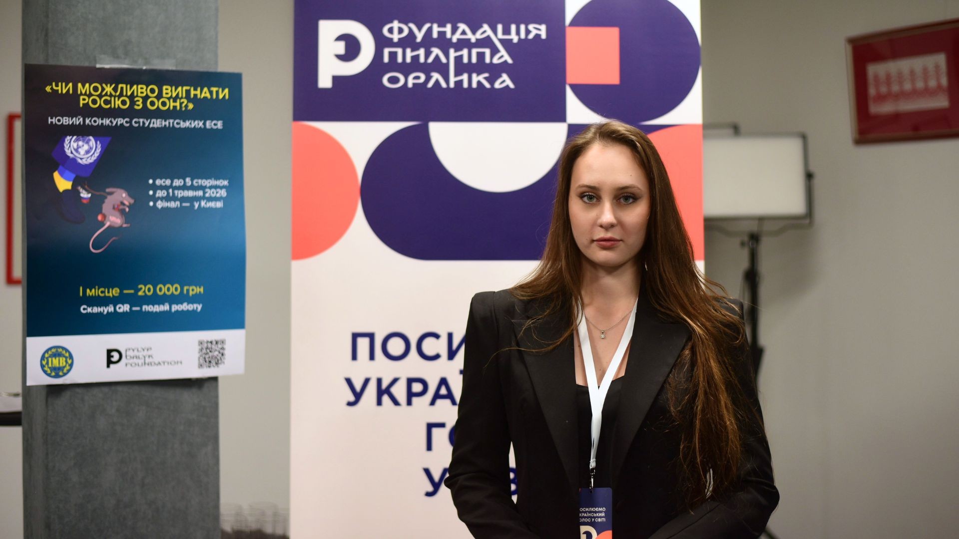 Катерина Опанасенко на заході Фундації Пилипа Орлика на тлі банеру конкурсу студентських есе «Чи можливо вигнати Росію з ООН?»