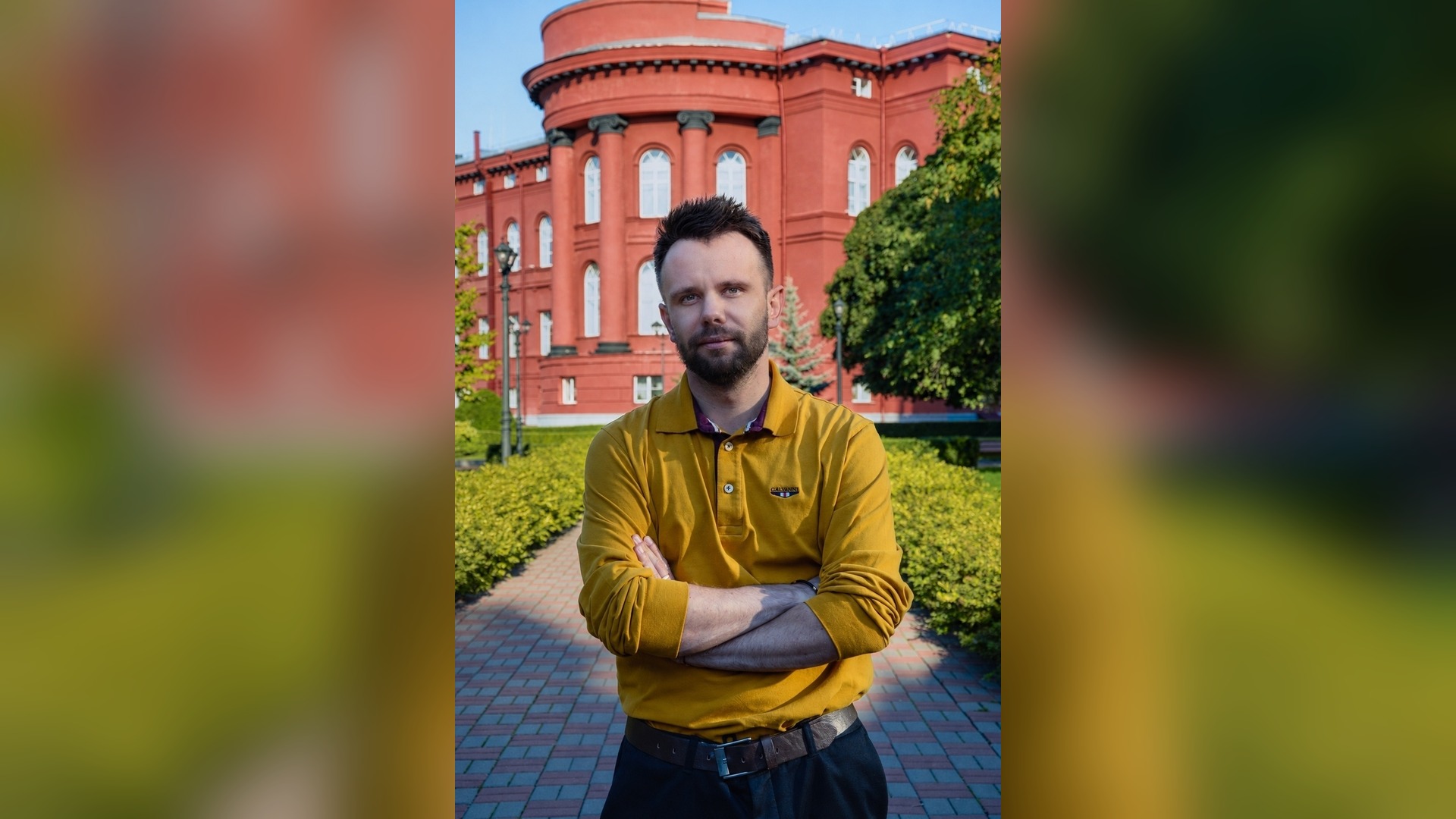 Petro Katerynych, PhD, lecturer at the Institute of Journalism of Taras Shevchenko National University of Kyiv, standing outdoors near a red university building