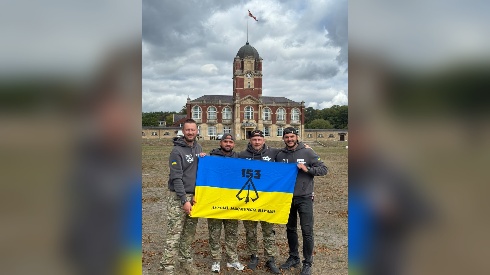 Servicemen of the 153rd Sniper Training Center with the flag of Ukraine against the backdrop of Sandhurst Academy