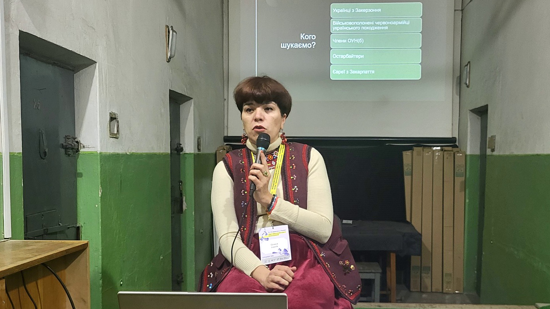 Олеся Ісаюк на фоні слайду «Кого шукаємо» зі списком категорій в'язнів Аушвіцу