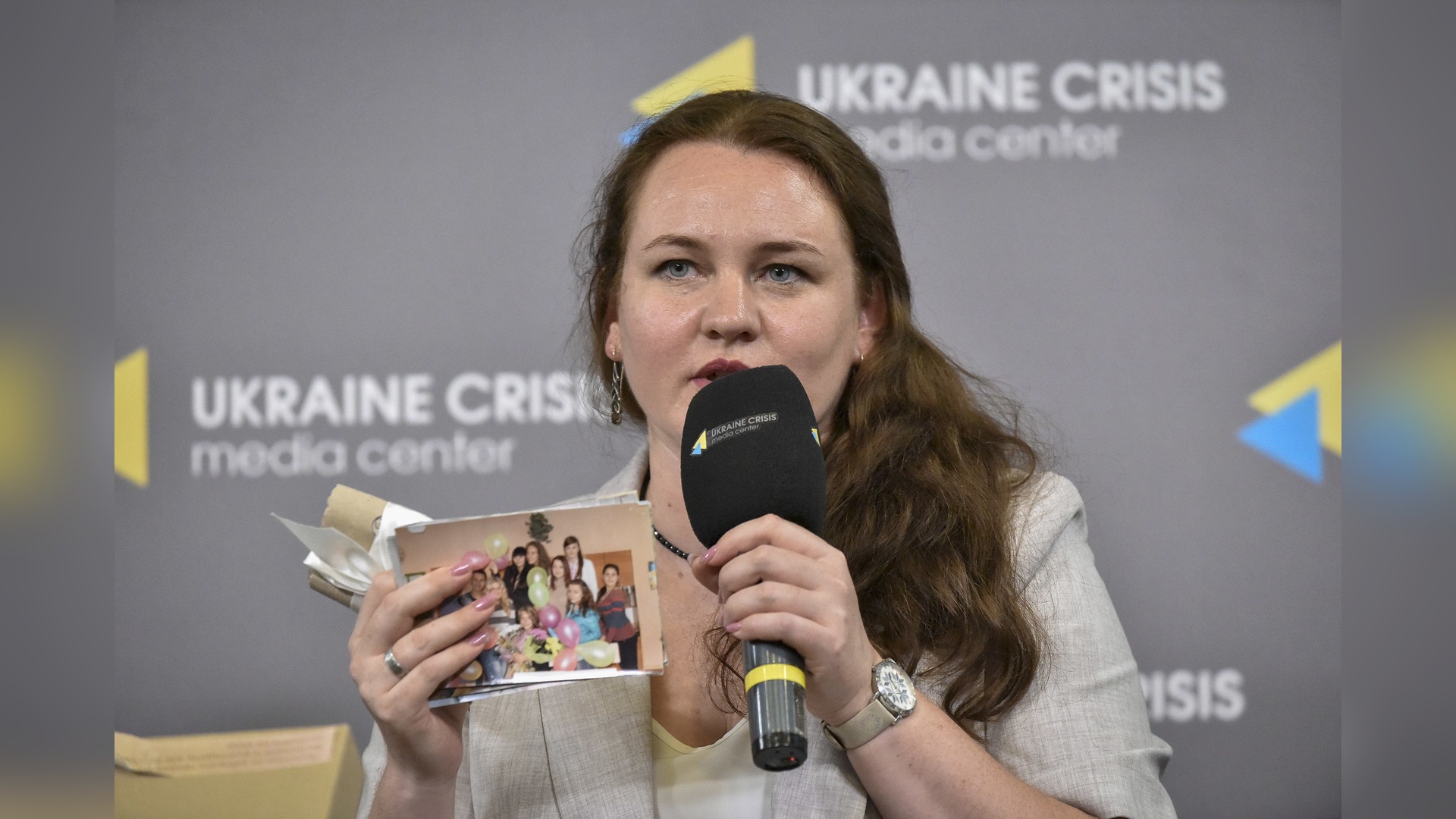 Наталя Омельчук тримає старі фотографії з луганської школи біля мікрофона