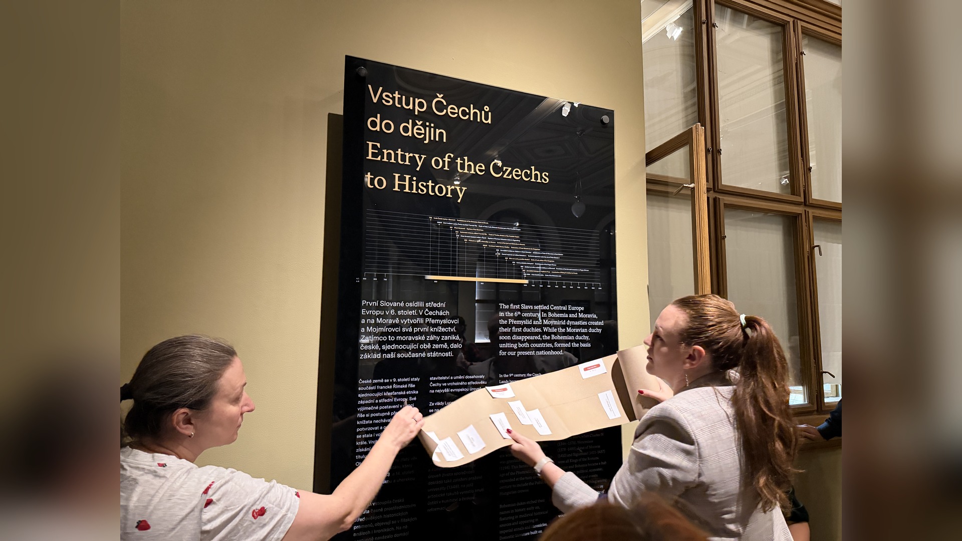 Two program participants hold a paper timeline with notes near the museum's information stand