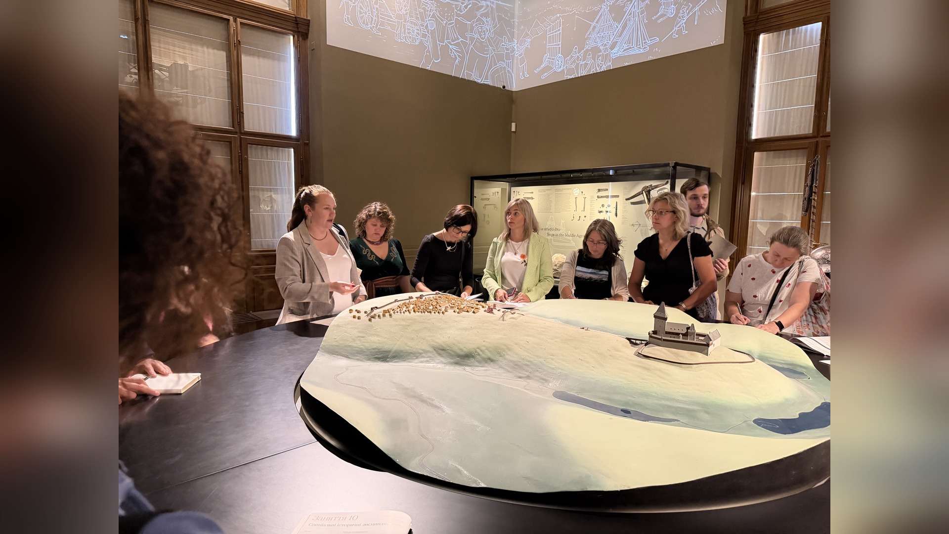 Program participants stand around a large model of a medieval city and castle, listening to explanations