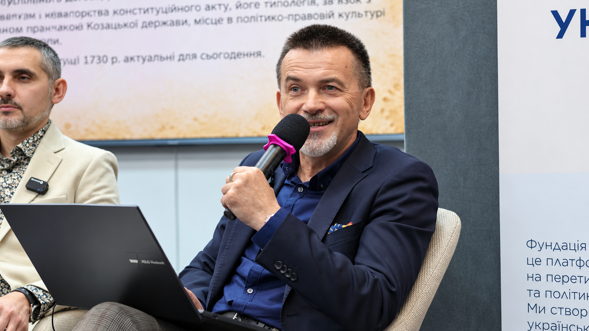 Historian Viktor Horobets with a microphone and laptop smiling during his presentation at the panel discussion