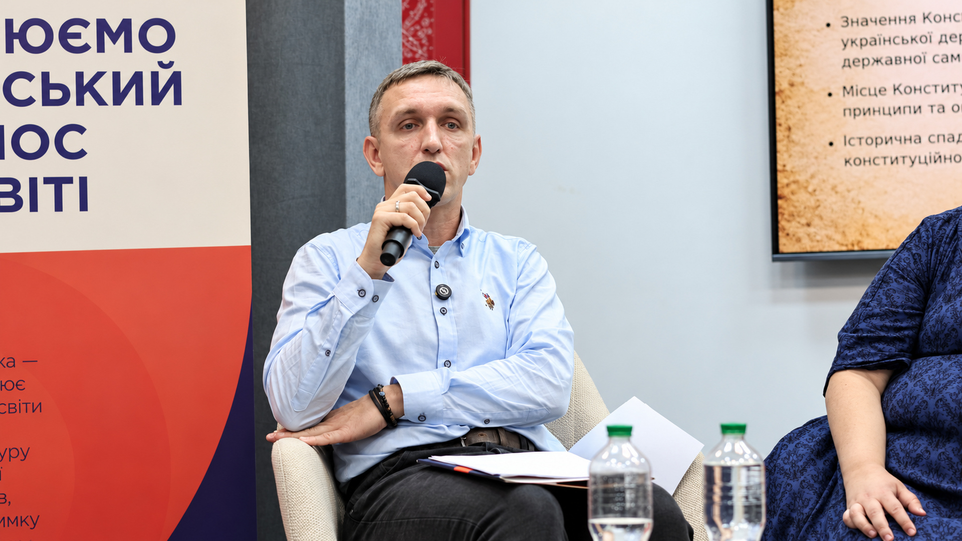 Oleksii Yushchenko in a light shirt speaking into a microphone during the panel discussion in Kyiv