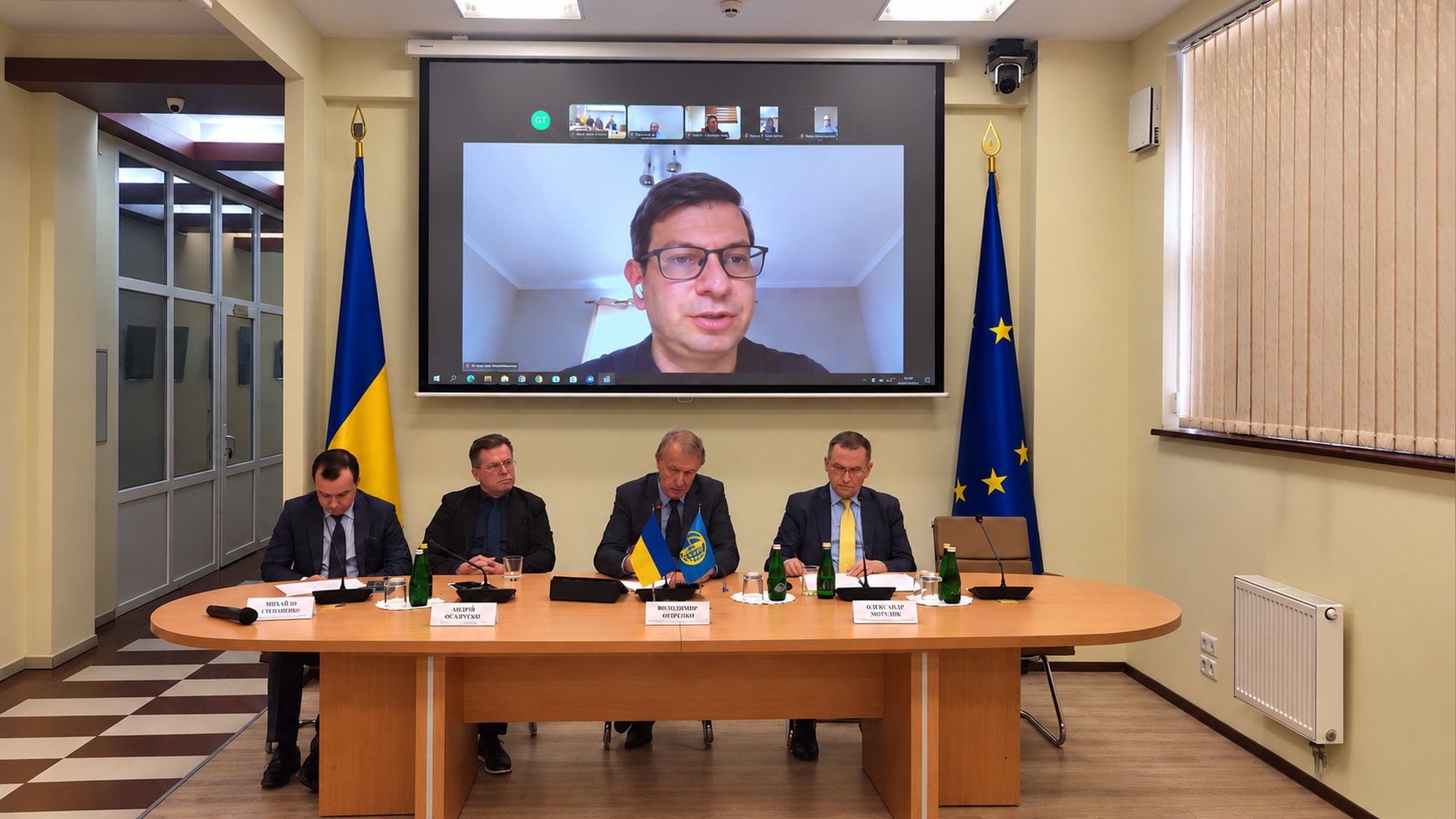 Максим Баришніков виступає по відеозв’язку на екрані проєктора над президією круглого столу про російські активи