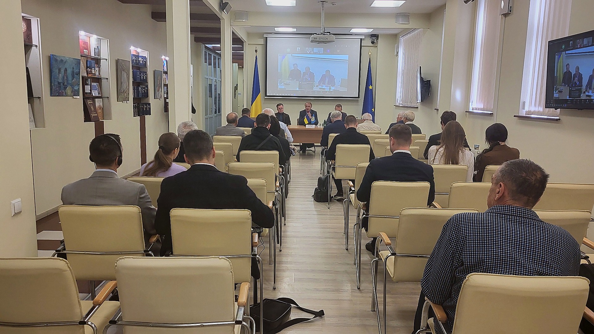 Зал круглого столу про російські активи: слухачі сидять спиною до камери, попереду президія та екран із відеозв’язком