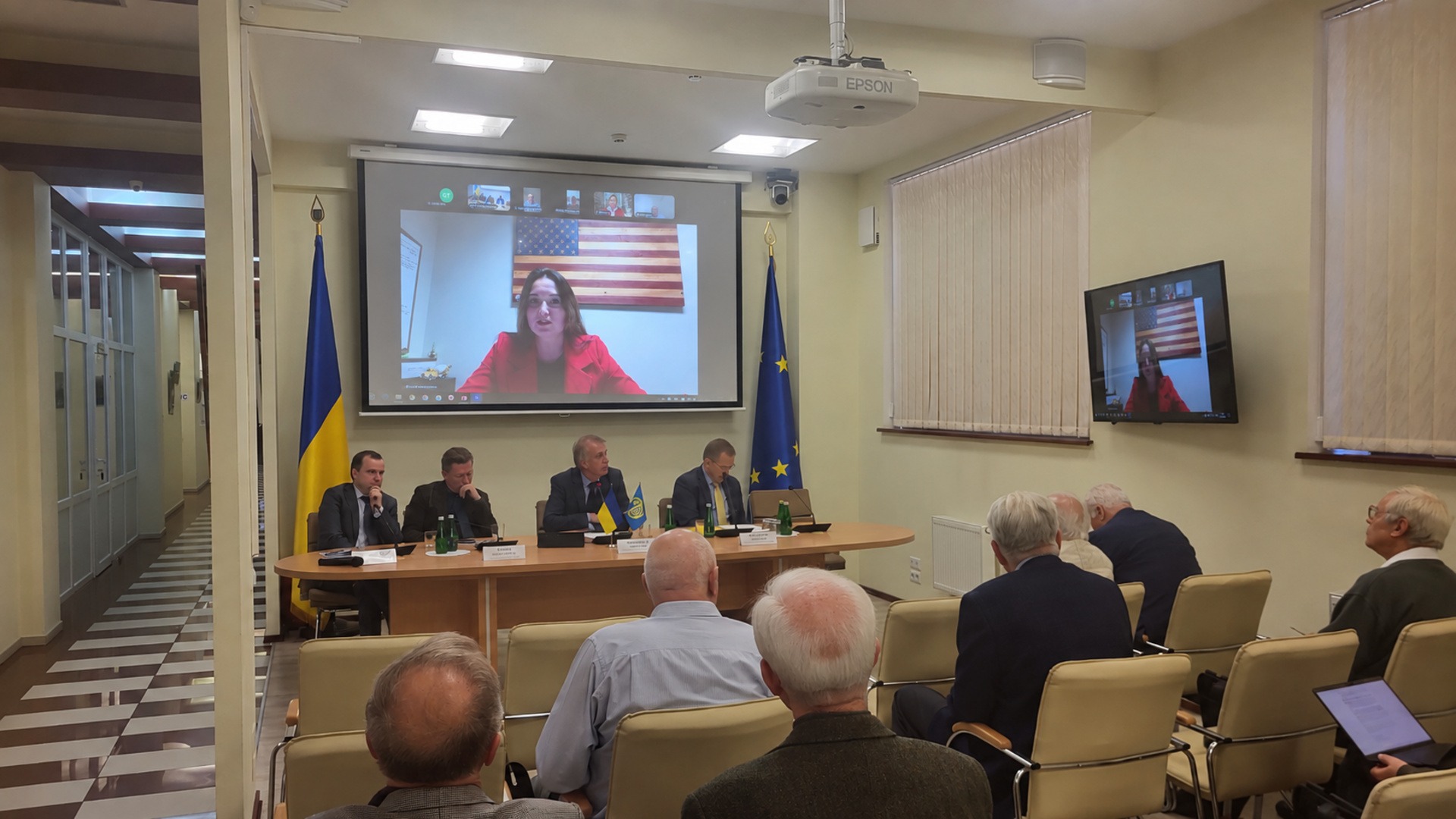Леся Яструбецька виступає по відеозв’язку на екрані проєктора над президією круглого столу про російські активи