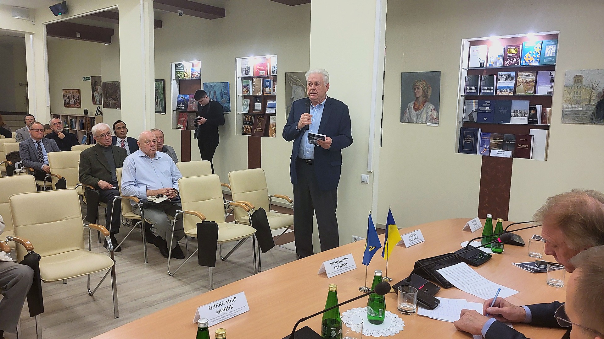 Володимир Єльченко стоїть із мікрофоном і виступає перед учасниками круглого столу про російські активи у Києві