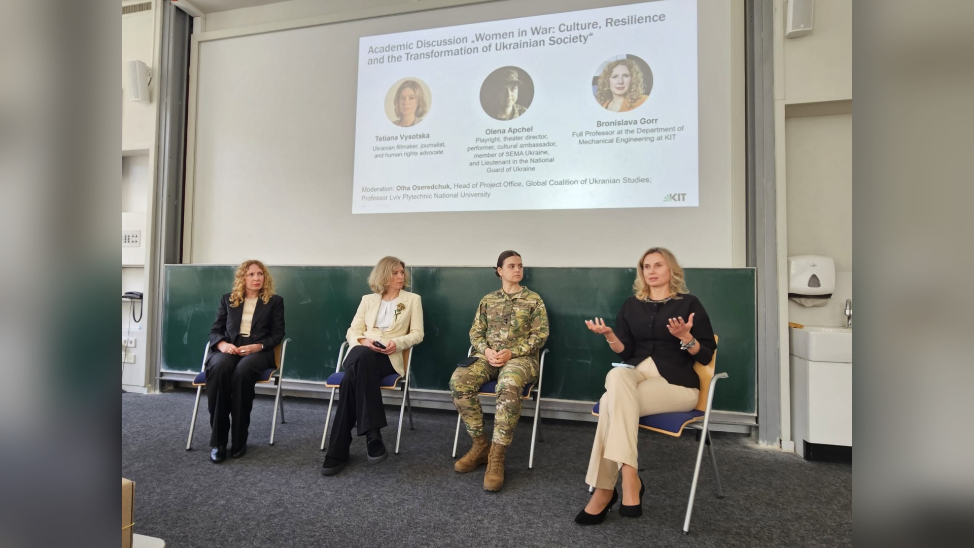 Чотири учасниці дискусії «Жінки під час війни» сидять перед екраном з програмою заходу в аудиторії Karlsruhe Institute of Technology