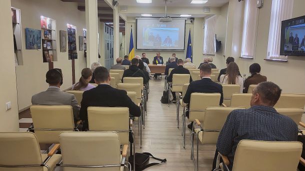 Зал круглого столу про російські активи: слухачі сидять спиною до камери, попереду президія та екран із відеозв’язком