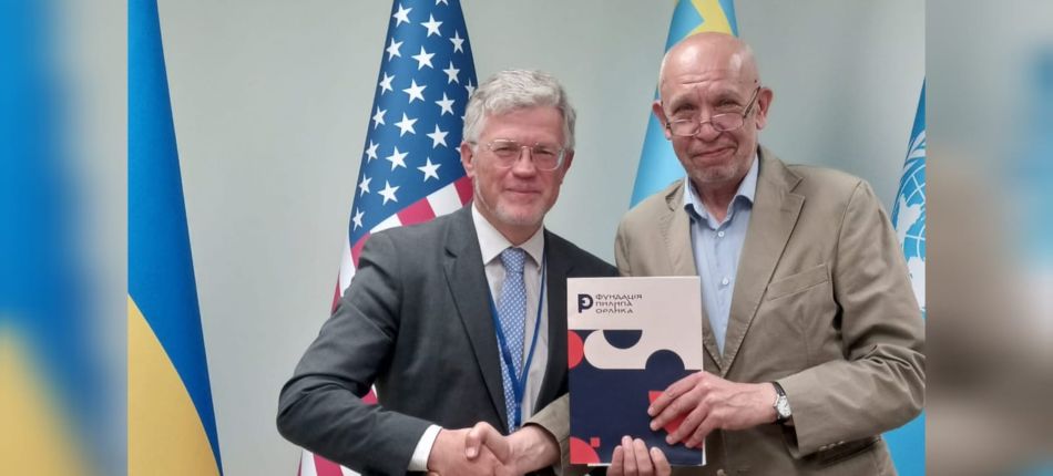 Постійний представник України при ООН Андрій Мельник та посол Ігор Харченко тиснуть руку у Нью-Йорку на фоні прапорів України, США та ООН