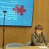 Олеся Ісаюк за столом представляє доповідь про ідентифікацію українців в Аушвіці, на екрані — слайд з пазлом