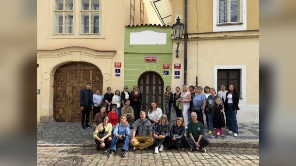 Група учасників менторської програми «Корені та крила» стоїть і сидить перед історичною будівлею Nejmenší dům у Празі