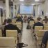 Зал круглого столу про російські активи: слухачі сидять спиною до камери, попереду президія та екран із відеозв’язком