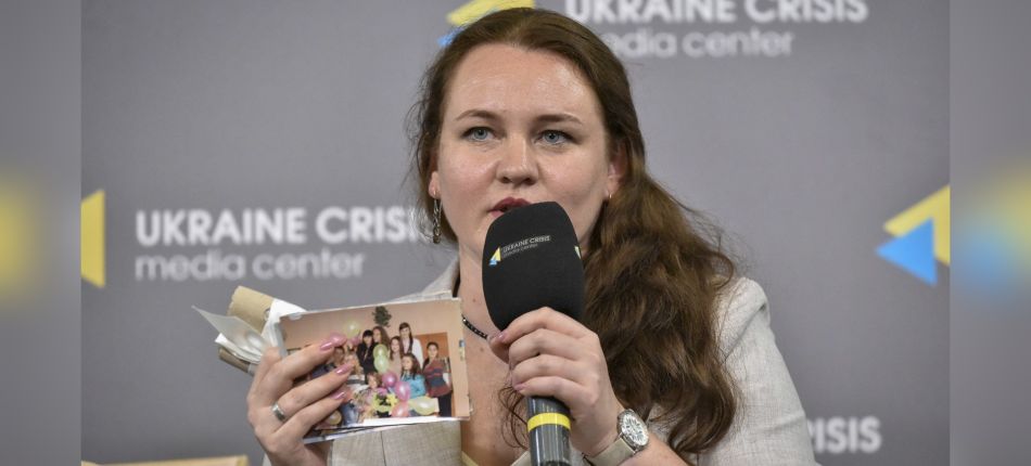 Наталя Омельчук тримає мікрофон і сімейні фотографії під час публічної дискусії про пам’ять Луганщини