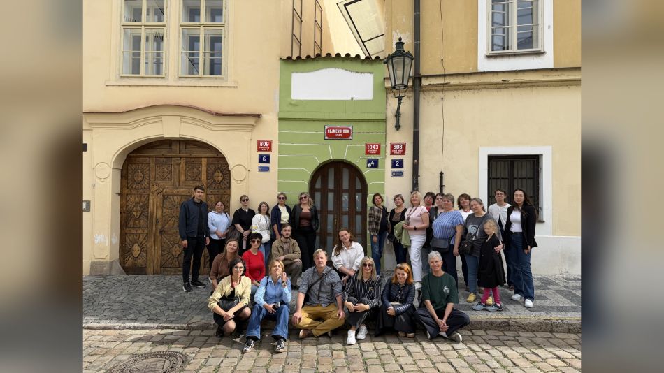 Група учасників менторської програми «Корені та крила» стоїть і сидить перед історичною будівлею Nejmenší dům у Празі