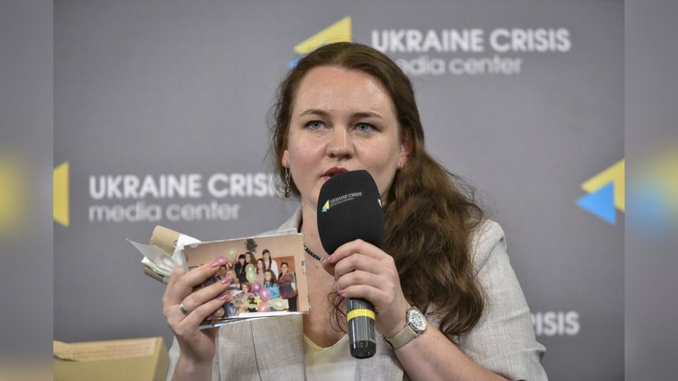 Наталя Омельчук тримає мікрофон і сімейні фотографії під час публічної дискусії про пам’ять Луганщини
