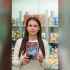 Ксенія Дворнікова тримає книгу «Вижити в Гостомелі: 21 історія з міста-героя» на тлі книжкових полиць