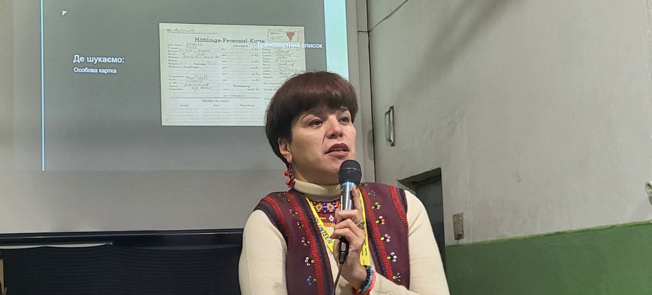 Олеся Ісаюк виступає з мікрофоном на лекції про ідентифікацію українців у списках в'язнів Аушвіцу
