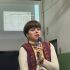 Олеся Ісаюк виступає з мікрофоном на лекції про ідентифікацію українців у списках в'язнів Аушвіцу