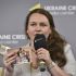 Наталя Омельчук тримає мікрофон і сімейні фотографії під час публічної дискусії про пам’ять Луганщини