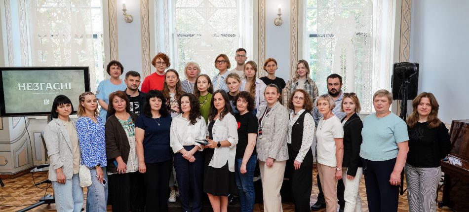 Учасники менторської програми Корені та крила стоять групою у залі бібліотеки на тлі екрана з написом Незгасні